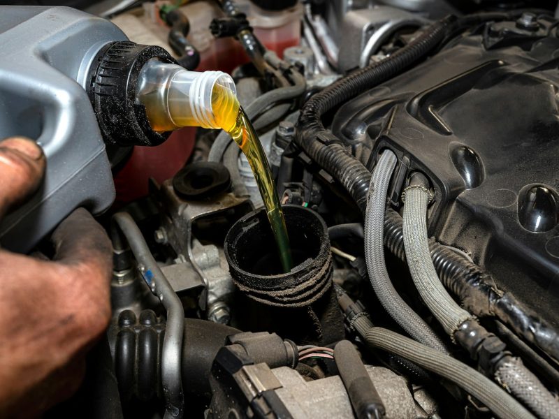 Car mechanic pours new car oil into the engine from a plastic tank in a car workshop. Car mechanic pours new car oil into the engine from a plastic tank in a car workshop.
